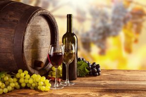 Red and white wine bottle and glass on wooden keg. Grapes of wine on background